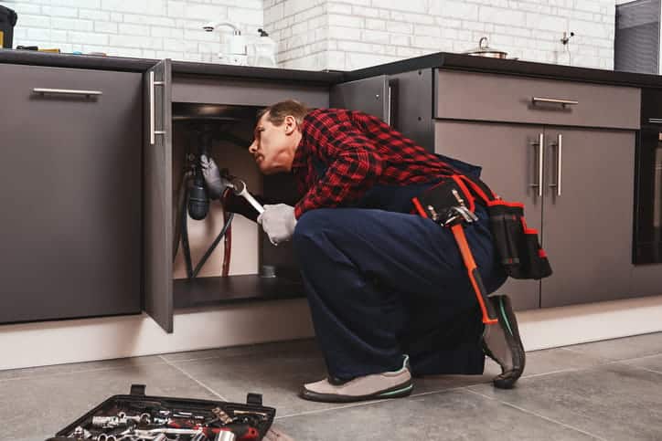 A plumber inspecting underneath a kitchen sink. 
